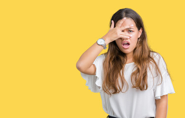 Young beautiful brunette business woman over isolated background peeking in shock covering face and eyes with hand, looking through fingers with embarrassed expression.