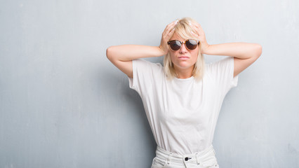 Adult caucasian woman over grunge grey wall wearing sunglasses suffering from headache desperate...