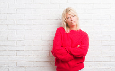 Adult caucasian woman over white brick wall wearing winter sweater skeptic and nervous, disapproving expression on face with crossed arms. Negative person.