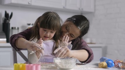Positive mother and joyful little daughter with special needs having fun and playing with flour while cooking together. Happy cooking family stained with flour from head to toe baking in the kitchen. - Powered by Adobe
