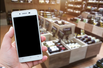 Men use hold smartphone blurred images of Various alcohol bottles in a row at the spirits store background.