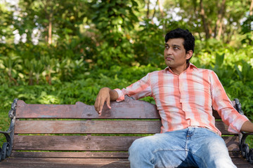 Indian man thinking while sitting on wooden bench in peaceful gr