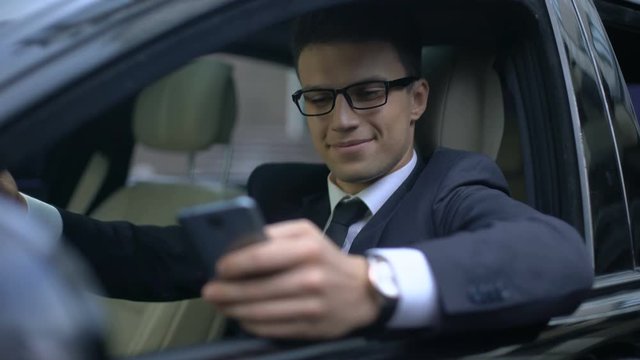 Happy businessman texting with girlfriend and smiling while sitting in car