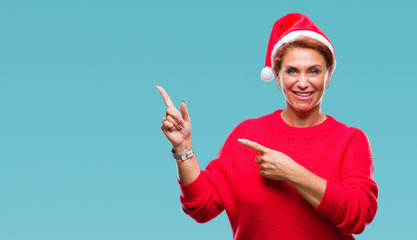 Atrractive senior caucasian redhead woman wearing christmas hat over isolated background smiling and looking at the camera pointing with two hands and fingers to the side.