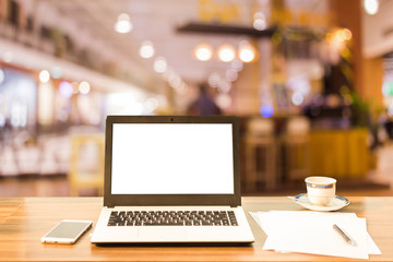 Mockup image of laptop with blank white screen on wooden table blurred images In the coffee shop at shopping mall background.