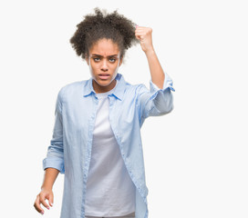 Young afro american woman over isolated background angry and mad raising fist frustrated and furious while shouting with anger. Rage and aggressive concept.