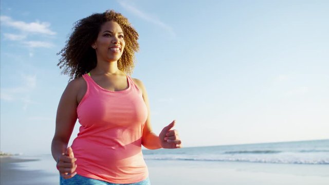 Happy afro hair African American female speed walking along the beach at sunrise for healthcare fitness training 