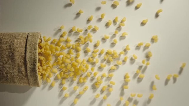 TOP VIEW: Bag falls and lumaconi pasta are poured out of it on white background - Slow Motion