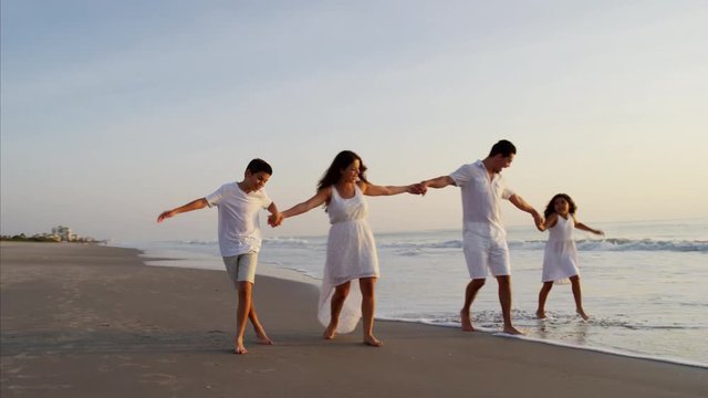 Attractive Latin American family walking on the ocean beach at sunrise