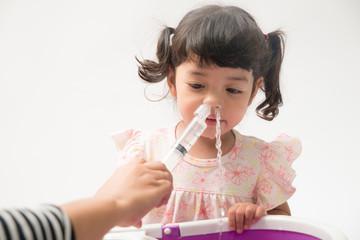 Asian mother making nasal wash for her baby girl by flushing kid'nose with syringe and saline. An Irrigation can benefit people who have sinus problems,nasal allergies isolated on white background - obrazy, fototapety, plakaty