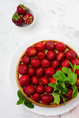 Cheesecake with fresh strawberries and mint on white plate on gray concrete background. Top view.