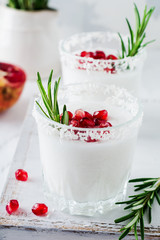 Christmas coconut punch with pomegranate seeds and sprigs of rosemary on light background. Selective fоcusе. Top view.