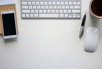 White wooden table with keyboard, pen, notebook, mobile phone and a cup of coffee. Workspace top view with copy space.