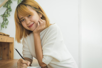 Naklejka premium Asian woman write shopping lists in notepad by pen on her kitchen counter at home and reading and tries to remember all ingredients to shopping in grocery. Lifestyle women relax at home concept.
