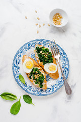 Fried spinach, egg and pine nuts sandwiches on light background. Delicious healthy breakfast or snack. Top view.
