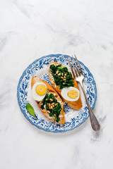 Fried spinach, egg and pine nuts sandwiches on light background. Delicious healthy breakfast or snack. Top view.