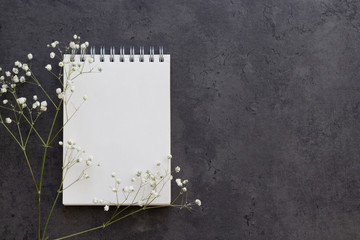 Notebook with and branche of little white flowers on the grey concrete background. Spring and Mother's Day concept. Top view, copy space, mock up