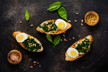 Fried spinach, egg and pine nuts sandwiches on brown vintage old concretebackground. Delicious healthy breakfast or snack. Top view.