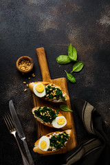 Fried spinach, egg and pine nuts sandwiches on brown vintage old concretebackground. Delicious healthy breakfast or snack. Top view.