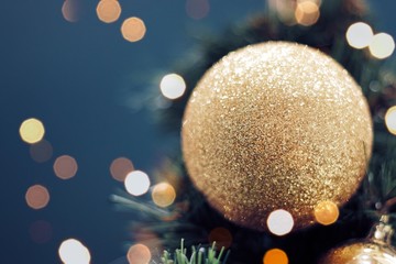 Closeup of gold bauble hanging from a decorated Christmas tree. Shiny happy new year concept.