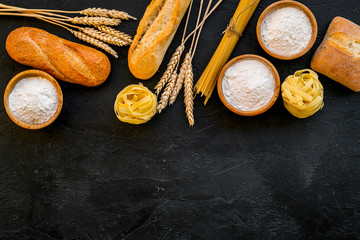 Bakery production, making bread and pasta. Fresh bread and raw pasta near flour in bowl and wheat ears on black background top view space for text