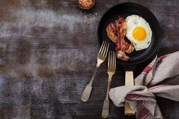 Foto op Plexiglas Spiegeleieren Traditioneel Engels ontbijt met gebakken eieren en spek in gietijzeren pan op donkere betonnen ondergrond. Bovenaanzicht.