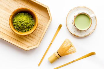 Coffee and cocktails with matcha concept. Matcha latte near bowl with matcha powder and whisk on wooden tray white background top view copy space