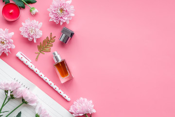 Perfume on feminine desk. Women's accessories. Perfume near notebook for dairy among flowers on pink background top view copy space