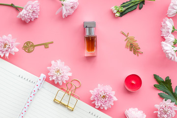 Perfume on feminine desk. Women's accessories. Perfume near notebook for dairy among flowers on pink background top view