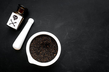 Prepare poison. Bottle with skull and crossbones near mortar and pounder on black background top view copy space