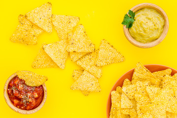 Snack for party. Mexican nachos near salsa and guacamole sause on yellow background top view