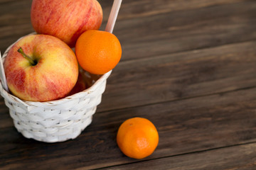 Apples and mandarins in white wicker basket on the wooden table. Close-up, copy space