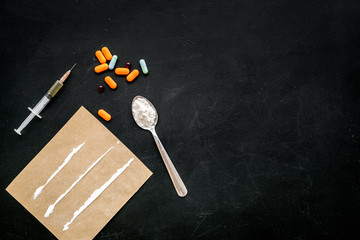 Take drugs, drugs addiction concept. White powder like heroine or cocaine, drug tracks pills, spoon, syringe on black background top view space for text