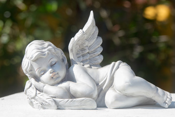 Sleeping of little cupid's ceramic doll on stone. Items for house, garden, and interior or exterior...
