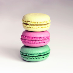 Yellow, pink and green macarons on the white table, toned. Close-up, front view, copy space