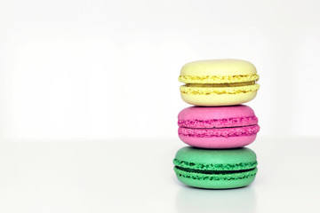 Yellow, pink and green french macarons on the white table. Close-up, front view, copy space