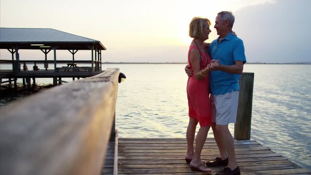 Happy senior Caucasian couple dancing on the pier at sunrise