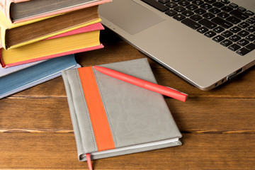 A stack of books, a notebook with a pen and a laptop on a wooden table. E-learning concept