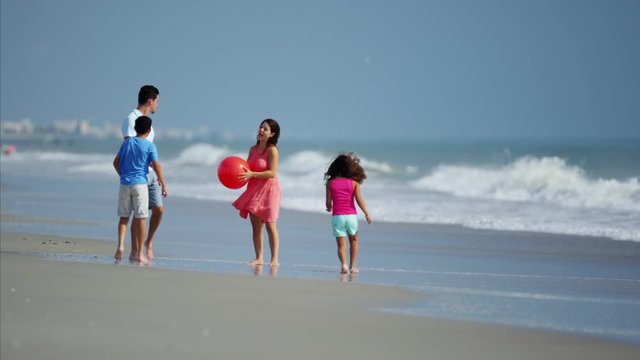 Young Hispanic family playing together on beach holiday with red ball