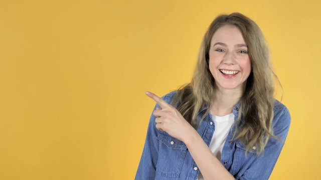 Portrait of Pretty Girl Pointing with Finger on Side, Yellow Background