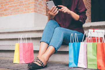 Consumerism, shopping, lifestyle concept, Young woman sitting near shopping bags and gift box while playing smartphone enjoying in shopping