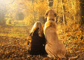 Beste Freunde Kind und Hund sitzen glücklich zusammen im leuchtenden Herbstwald