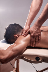 side view, two young man, 20-29 years old, sports physiotherapy indoors in studio, photo shoot. Physiotherapist massaging patient shoulder with his hands close-up.