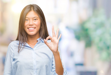 Fototapeta premium Young asian business woman over isolated background smiling positive doing ok sign with hand and fingers. Successful expression.