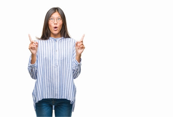 Young asian woman over isolated background amazed and surprised looking up and pointing with fingers and raised arms.