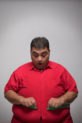 Obese man measuring his overweight belly with a measuring tape expressing surprise