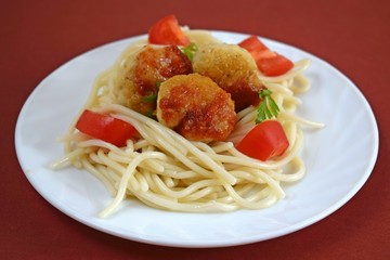 Delicious spaghetti with meatballs with tomatoes and herbs on a white plate.