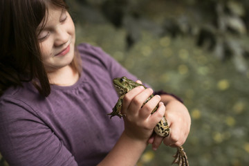 child holding frog in hands, studies and examines