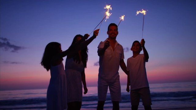 Hispanic family having fun at sunset with sparklers on the beach by the ocean