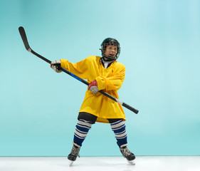 A hockey player in uniform with equipment over a blue studio background. The athlete, child, sport,...